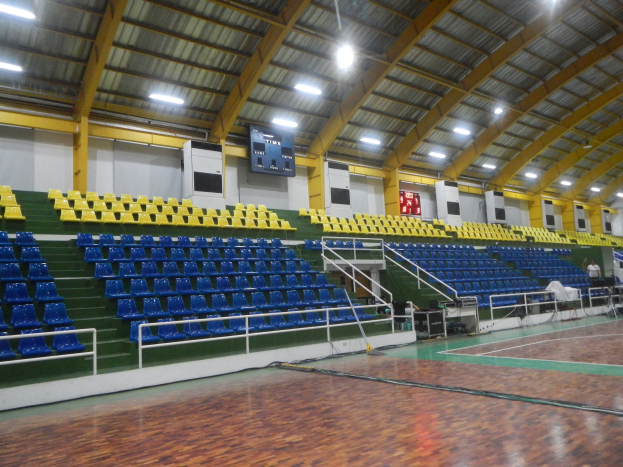 Große Halle mit Holzboden, blauen und gelben Sitzplätzen, Geländern, Treppen zum Sitzbereich, Wandbildschirmen, Deckenleuchten und einigen Personen.