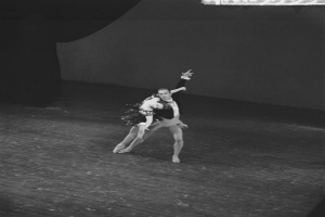 Ein Schwarz-Weiß-Foto eines Paares, das anmutig auf einer Bühne tanzt, ihre Arme ineinander verschlungen, mit einer Wand im Hintergrund.