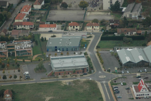 Eine Vogelperspektive auf ein dicht bebautes Stadtgebiet mit zahlreichen Gebäuden, Straßen voller Fahrzeuge, geparkten Autos und zwischendurch Bäumen und Gärten.