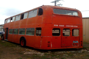 Ein roter Doppeldeckerbus parkt vor einer Hütte und einem Strommast.