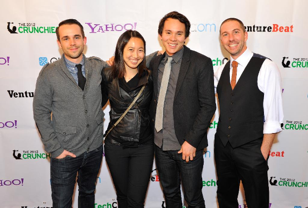 Eine Gruppe strahlender Personen, die für die Kamera posieren und im Hintergrund ein Sponsorenbanner halten.