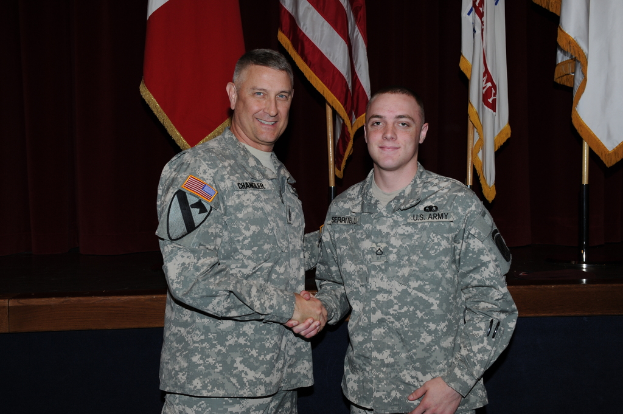 Zwei Personen in Uniformen geben sich die Hand und lächeln, vor vier Flaggen auf dunklen Hintergrund.