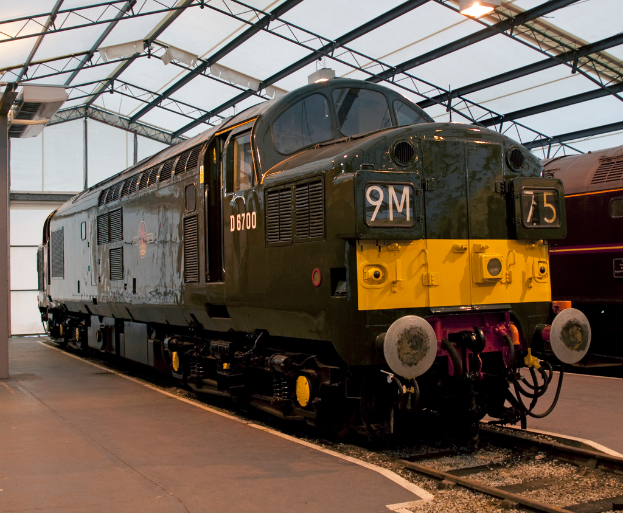 Ein Zug steht auf den Schienen neben einer Plattform mit einem am Dach befestigten Mast.