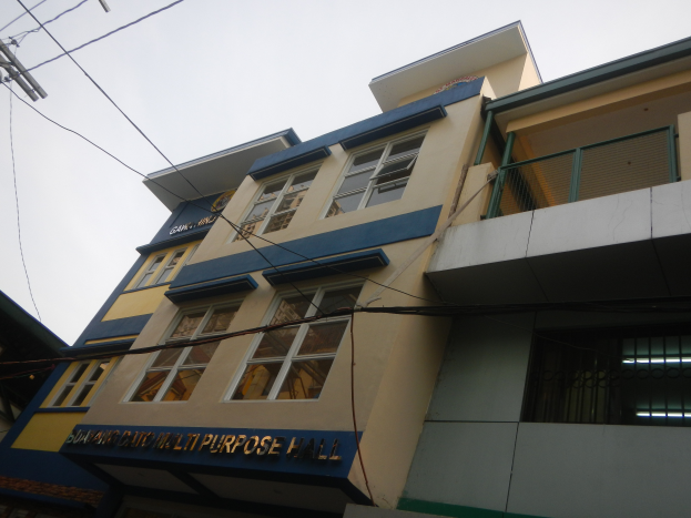 Ein mehrzweckgebäude mit blauer und gelber Fassade, Glasfenstern, einem Namensschild, einem elektrischen Mast mit Drähten und einem klaren blauen Himmel im Hintergrund.