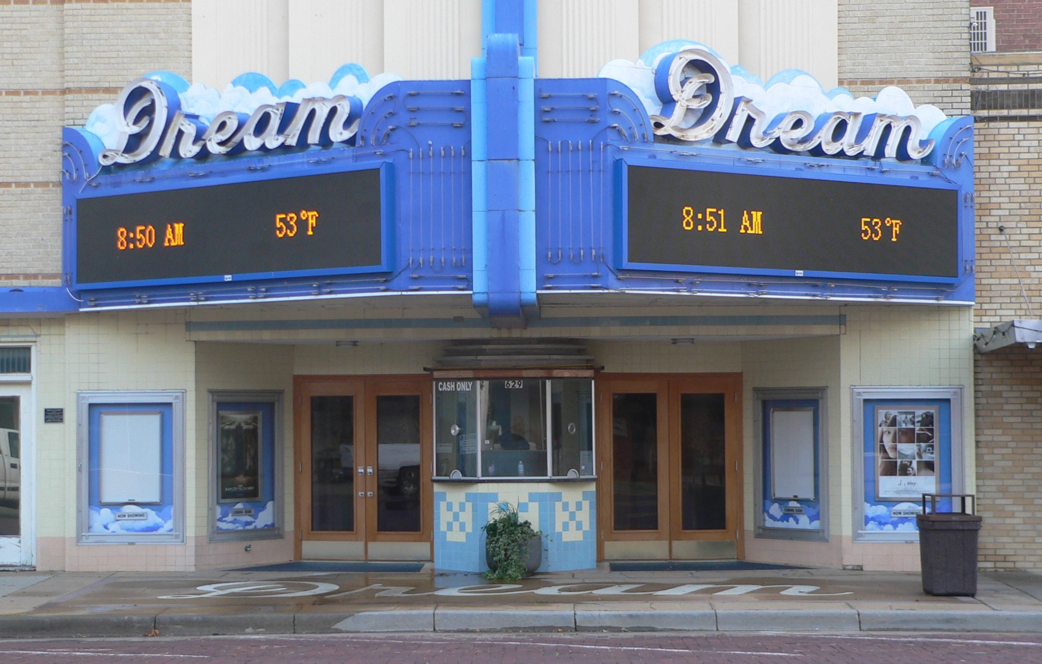 Außenansicht des Dream Theaters in St. Louis, Missouri, mit Glasfenstern und -türen, einem Namensschild, einem Mülleimer, einem Topf mit einer Pflanze und einer Straße im Vordergrund.