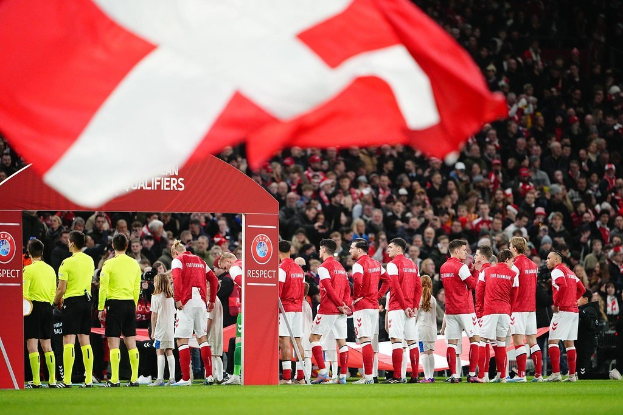 Gruppe von Menschen auf einem Fußballfeld mit einer roten und weißen Flagge im Vordergrund, einem Bogen mit der Aufschrift "Bayern München vs Bayern München Wetten & Vorschau" im Hintergrund und einer großen Stadionmenge.