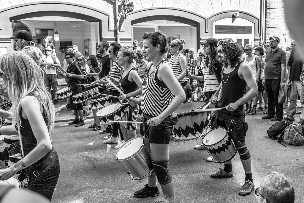 Eine Gruppe von Menschen, die Musikinstrumente auf der Straße spielen, vor einer geschlossenen Glastür mit einer Lampe im Hintergrund.