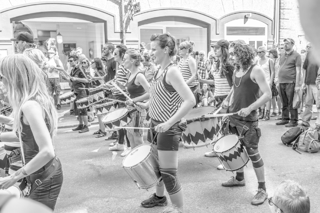 Eine Gruppe von Menschen, die Musikinstrumente auf der Straße spielen, vor einer geschlossenen Glastür mit einer Lampe im Hintergrund.