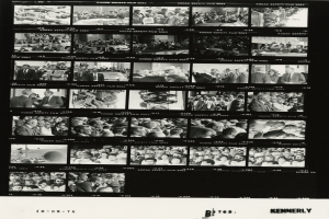 Schwarzes und weißes Foto einer vielseitigen Menschenmenge, die fröhlich in eine Fernsehbildschirm schaut, mit Text unten.