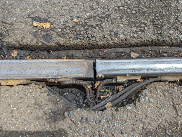 Nahaufnahme eines Metallkanalrohrs an der Seite einer Straße mit daran befestigten Drähten und trockenen Blättern in der Nähe.